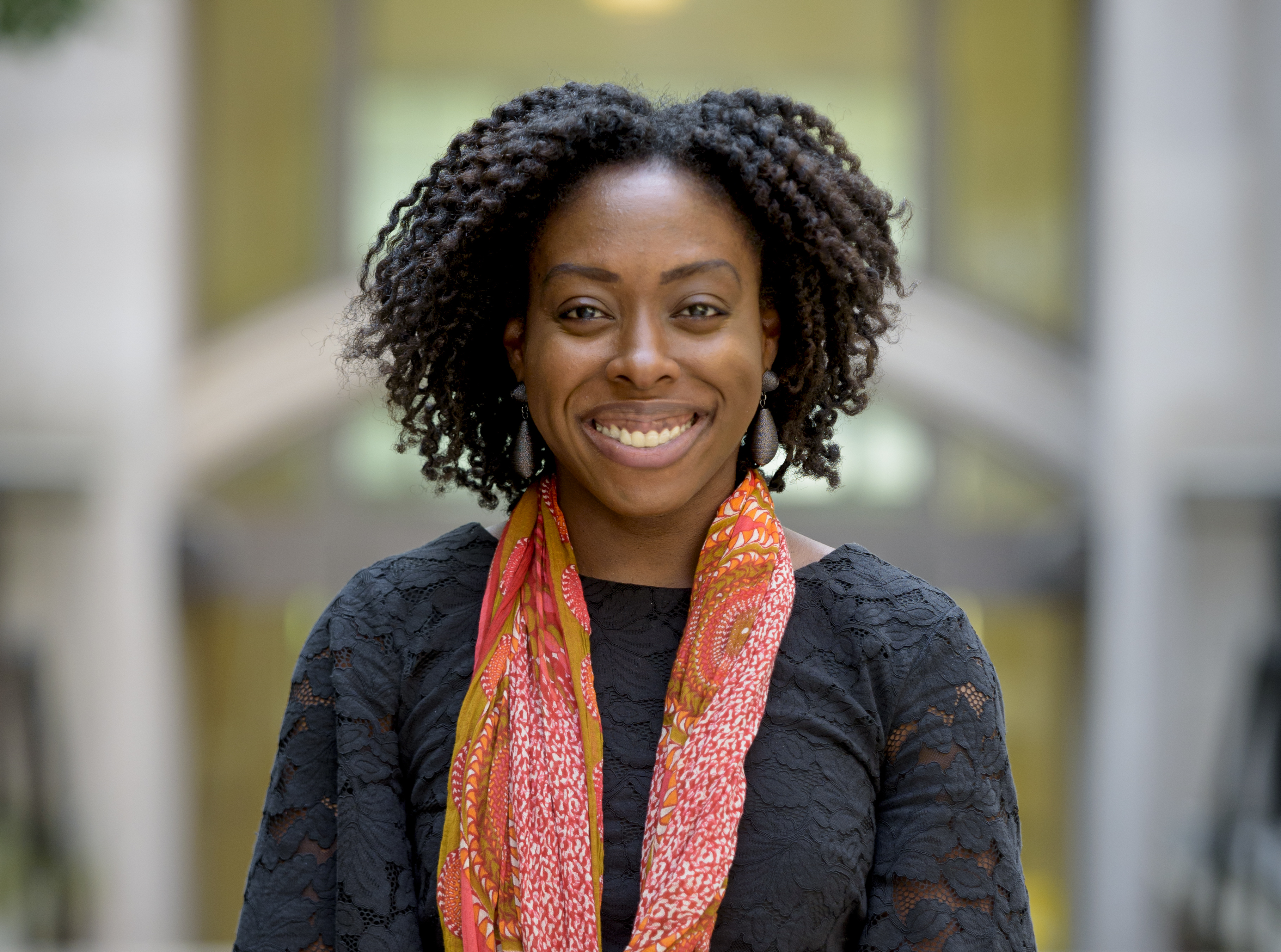 headshot of robin with curly hair, smiling outside, wearing a  flowered shirt and printed scarf